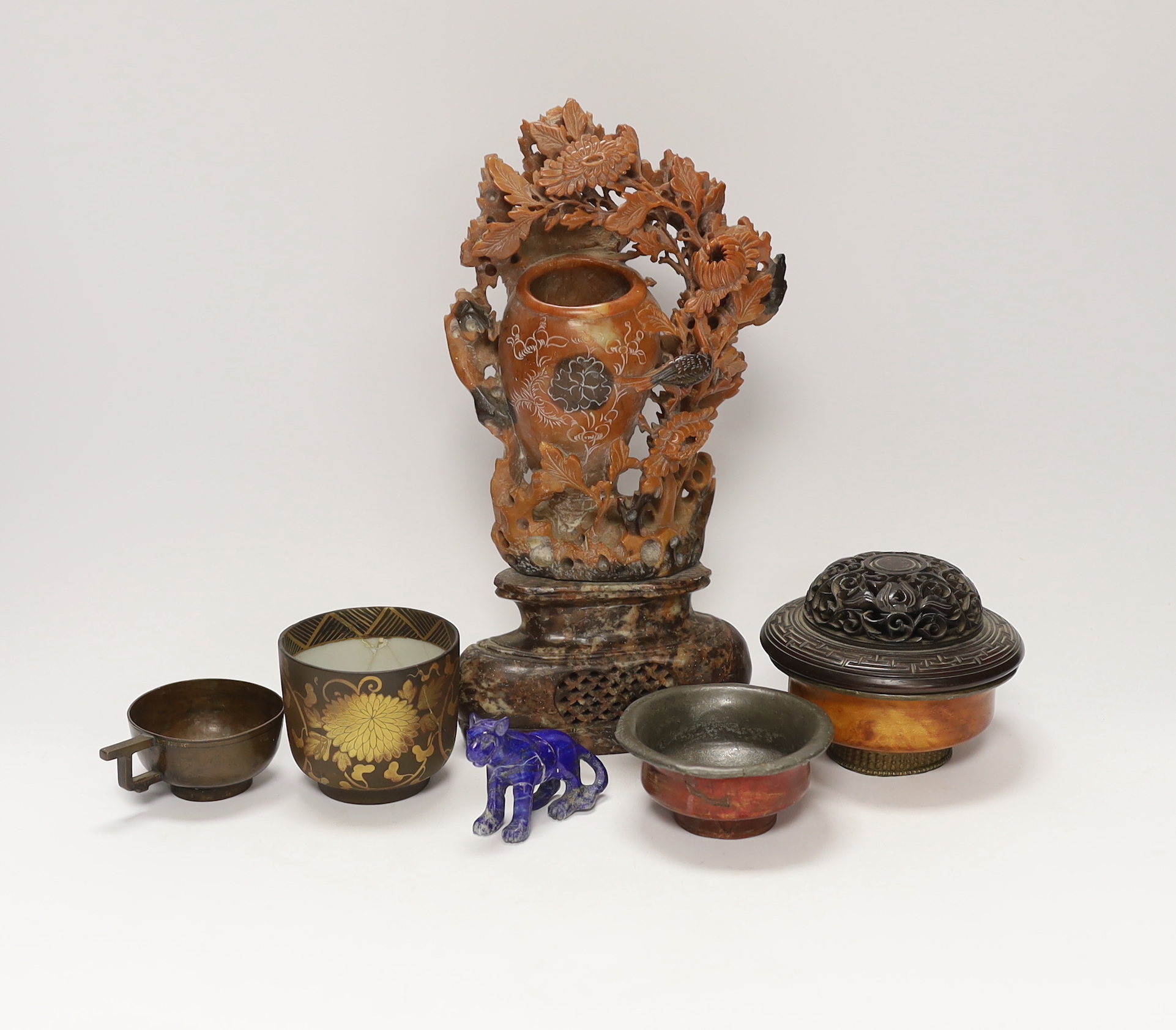 A Chinese carved hardwood cover, a soapstone carving, 27.5cm high, a lapis lazuli model of a tiger, a bronze teacup and two pewter and wood tea bowls (7)